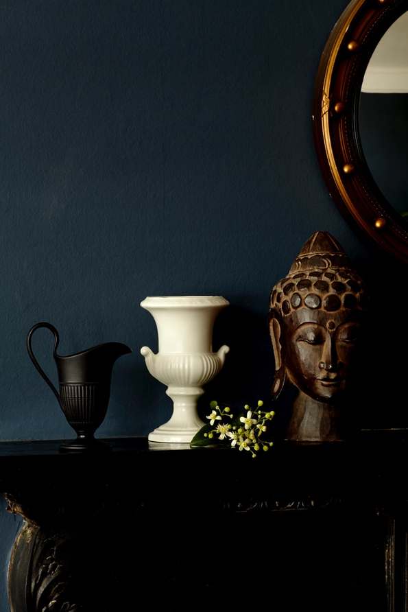 still life: black urn, white vase, buddha head on mantel next to round mirror