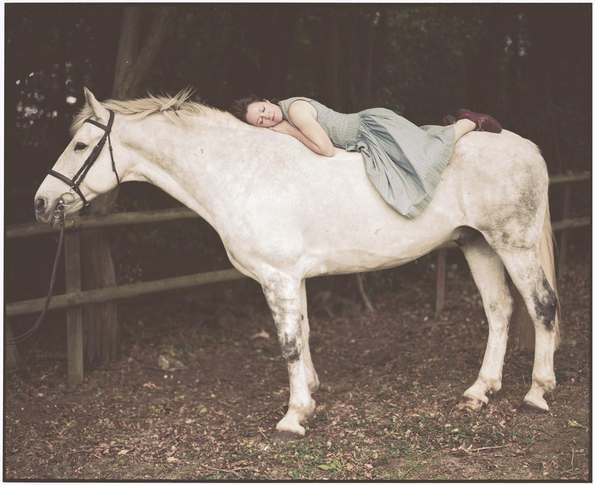 Woman sleeping on white horse in the woods